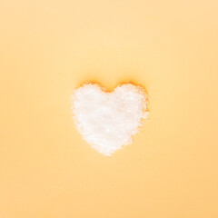 Heart made of snow on yellow background. Valentines day concept. Top view, flat lay