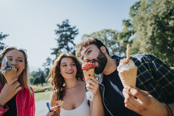 Obraz premium Carefree friends enjoying a sunny day in the park, eating ice cream, and having fun conversations. They create joyful memories in nature, embracing the positive energy of their leisure time together.