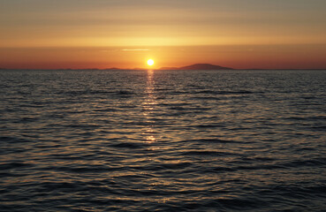 Pale and pastel colors of sea surface with waves and sundown on the horizon