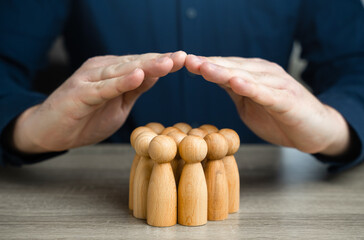 A man covers a group of people figures with house roof gesture. The concept of insurance and social...