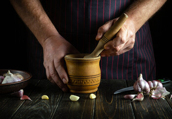 An experienced chef crushes garlic on the kitchen counter in a mortar before adding it to food....