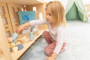Little girl playing alone in the kindergarten with wooden toys