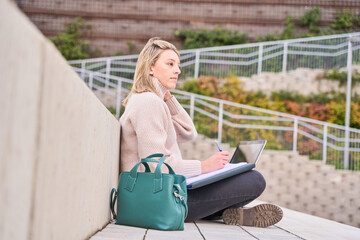 university student sitting on a campus bleachers studying or writing in her notebook.