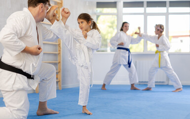 Fototapeta na wymiar Focused preteen girl in white kimono practicing karate kicking techniques during sparring with father. Sports family activity concept
