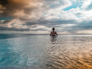 Back view of a woman standing in an infinity pool at sunset at Fuerteventura, Spain 