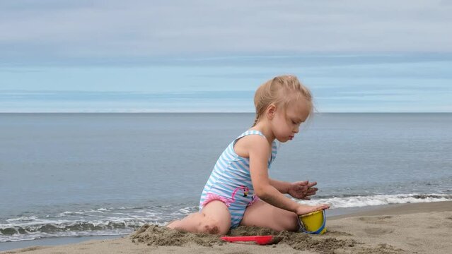 A little girl is playing on the seashore with sand and a bucket.