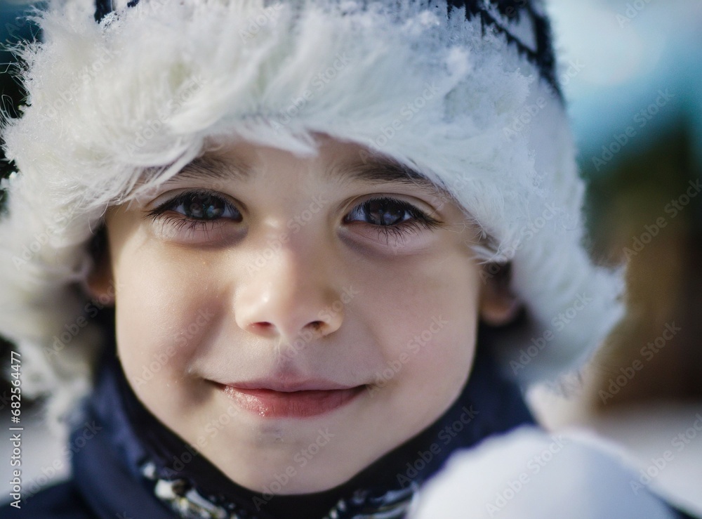 Wall mural Cute adorable child on Christmas holiday, face smiling wearing winter clothes, snow fur hat, face closeup portrait, cold snow, seasonal concept, outdoors scene