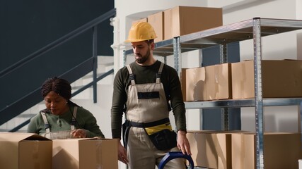 African american manager in warehouse next to assistant sealing cardboard box package ready to be...