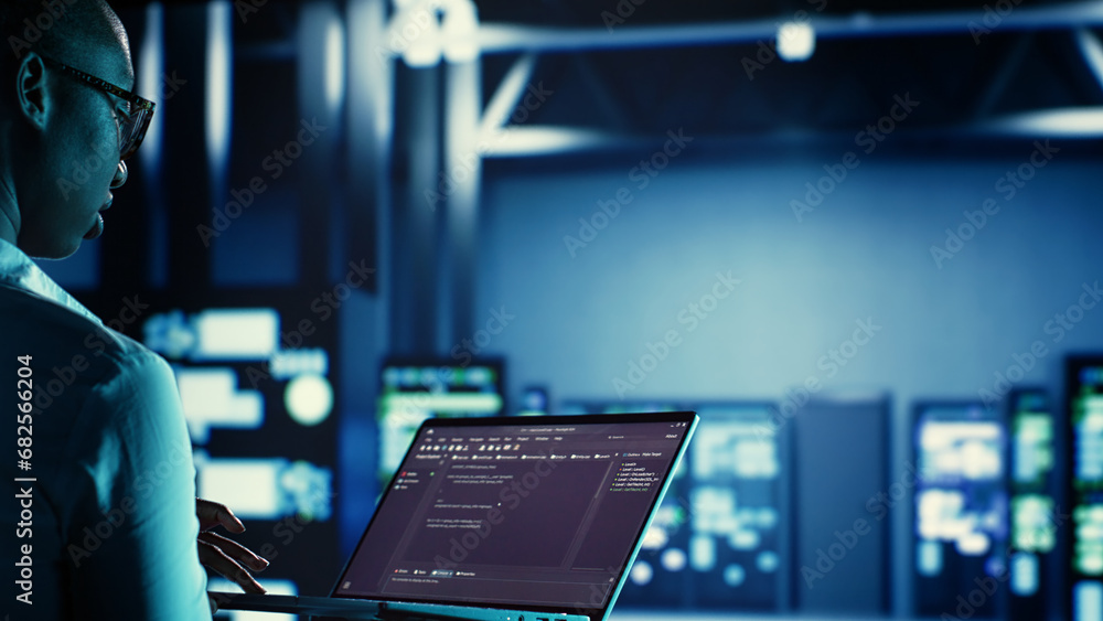 Poster manager overseeing data center, running code on laptop, troubleshooting and upgrading technologicall