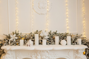 Luxury white fireplace with Christmas decoration, fir branch, candles, xmas glittering baubles, shiny flowers ornaments. Festive wall with illuminate garland warm lights . New year 2024 holidays.