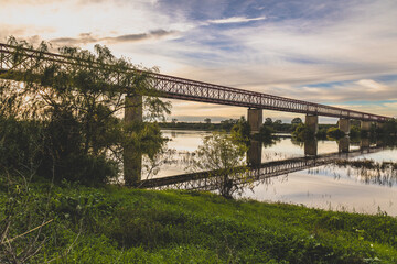 Fototapeta premium Old steel bridge at sunset. Bridge over the Tagus river, in the portuguese village of Chamusca - Ribatejo - Portugal. Bridge Isidro dos Reis - Chamusca