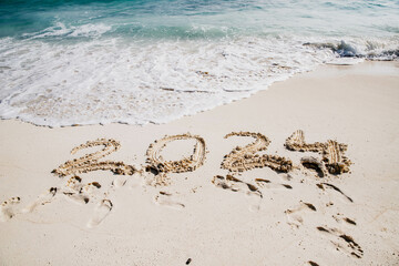 2024 written in white sand on tropical beach, happy New Year