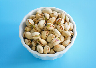Bowl or dish of raw organic pistachios that are salted and roasted on a bright background