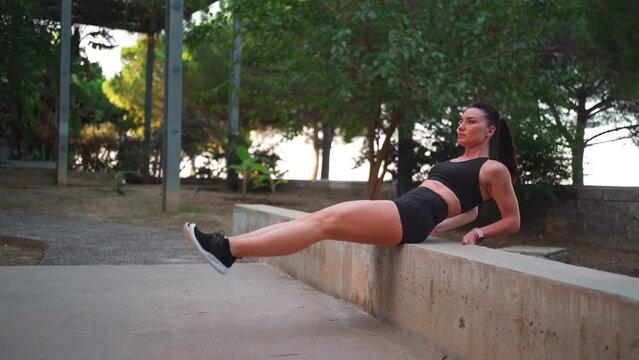 Woman doing abdominal exercise in park. Female athlete doing abs workout routine outdoors. Sportswoman practicing seated knee up raises exercise for abs. Healthy lifestyle concept