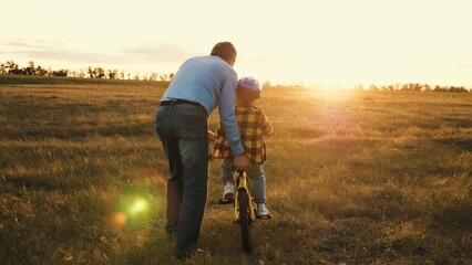 Supportive father gives gentle push to help persistent son steer bicycle - obrazy, fototapety, plakaty