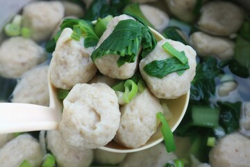 Close up photo of meatball soup with vegetable topping being lifted with a large ladle