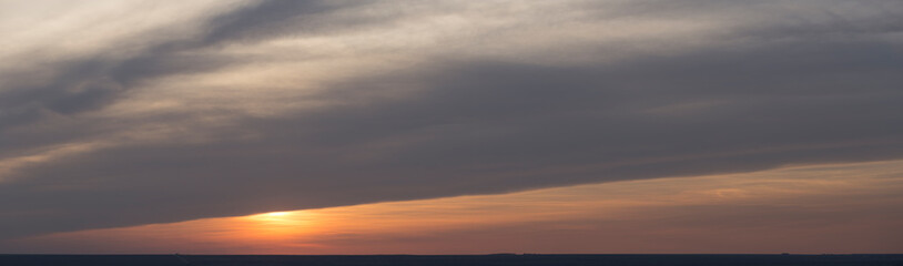 Fototapeta premium Landscape with bloody sunset. Panorama. Tragic gloomy sky. The last flashes of the sun on the storm clouds.