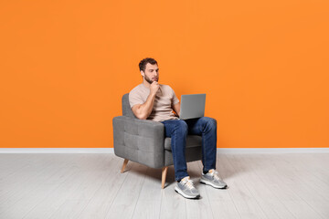Young man using laptop while sitting in armchair indoors
