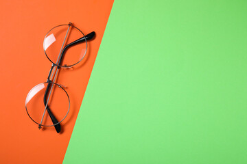 Glasses in stylish frame on color background, top view. Space for text