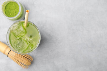 Glass of delicious iced green matcha tea, powder and bamboo whisk on light grey table, flat lay. Space for text