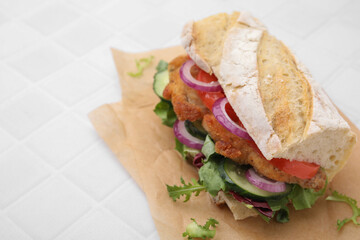 Delicious sandwich with schnitzel on white tiled table, closeup. Space for text
