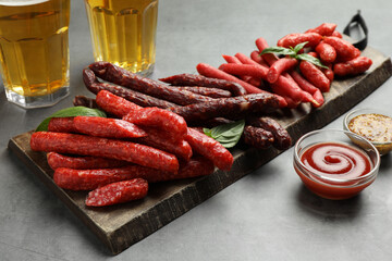 Different thin dry smoked sausages, sauces and glasses of beer on grey table