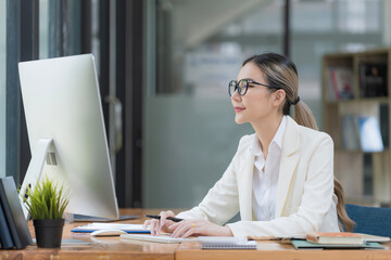 Portrait of a beautiful Asian businesswoman using a desktop computer, businesswoman managing company operations, analyzing statistics, commerce data, and marketing plans.