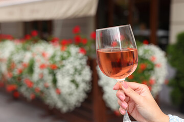 Woman holding glass of rose wine outdoors, closeup. Space for text