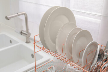 Drying rack with clean dishes near sink in kitchen, closeup