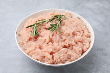 Fresh raw minced meat and rosemary in bowl on light grey textured table, closeup