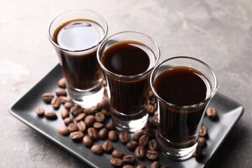 Shot glasses with coffee liqueur and beans on light grey table, closeup