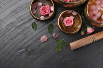 Tibetan singing bowls with water, beautiful rose flowers and mallet on gray table, flat lay. Space for text