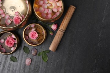 Tibetan singing bowls with water, beautiful rose flowers and mallet on gray table, flat lay. Space...