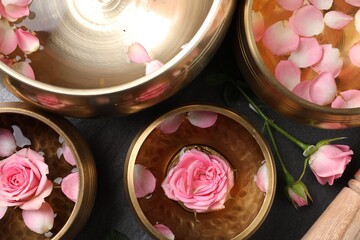 Tibetan singing bowls with water and beautiful rose flowers on table, flat lay