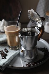 Brewed coffee in moka pot, glass of drink and beans on table
