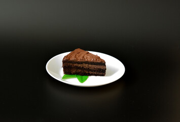 A piece of chocolate puff biscuit cake with mint leaves on a white ceramic plate on a black background.