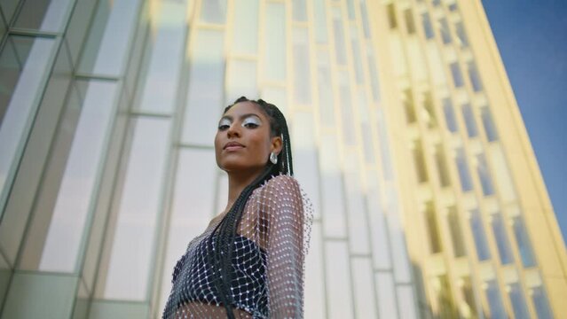 City fashionista walking street low angle. Dark skin lady touching braids posing