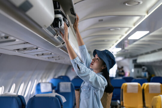 Young woman putting luggage into overhead locker on airplane. Traveler placing carry on bag in overhead compartment in aircraft