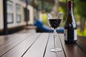 A glass of red wine with bottle put on wooden table at balcony of the house to enjoy and relaxing moment.