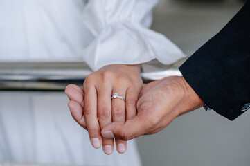The couple held hands in a very romantic way, the woman's hand was wearing a wedding ring and white clothes while the man was wearing black clothes