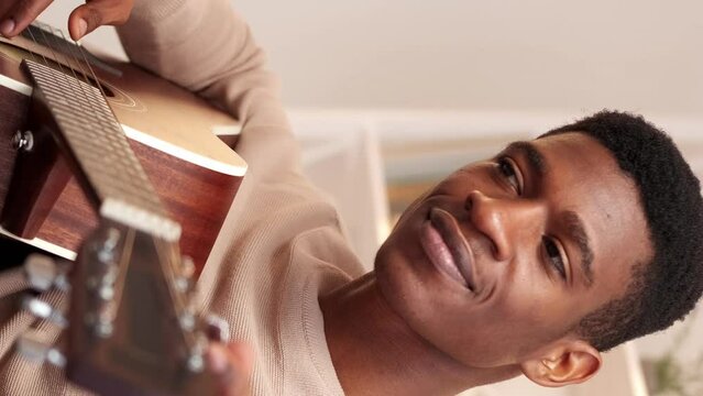 Vertical video. Guitar tuning. Music hobby. Song performance. Happy man adjusting pegs and gears playing string acoustic instrument enjoying home leisure.