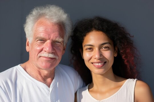 Smiling senior caucasian man posing with a young woman looking at the camera smiling