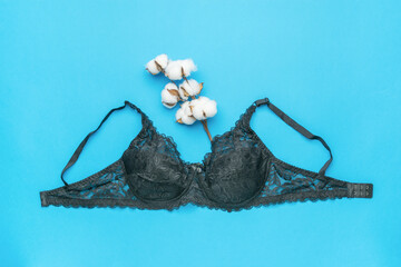 Classic black bra with a sprig of cotton on a blue background.