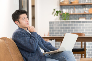 リモートワークやお洒落な自宅、カフェでパソコンをして考えたり悩んだりする男性