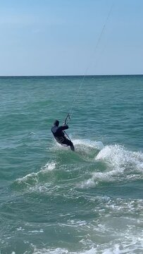 Adventurous man kiteboarding on sea waves. Male is enjoying water sport during summer vacation. Scenic view of seascape against sky. 