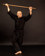 Portrait of aikido sensei master with black sensei belt in taekwondo kimono with bokken on black...