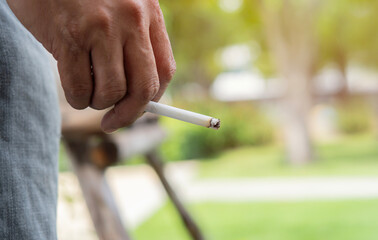 Image of cigarette in man hand with smoke while standing at outdoor.