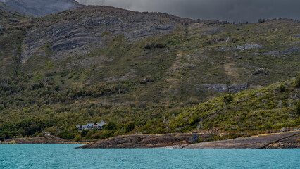 Landscape of Patagonia. In the foreground is a turquoise glacial lake. A house is visible in the...