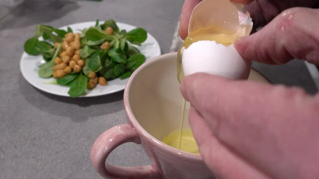 A male cook cracks an egg on a kitchen counter into a cup and separates the white from the yolk. 