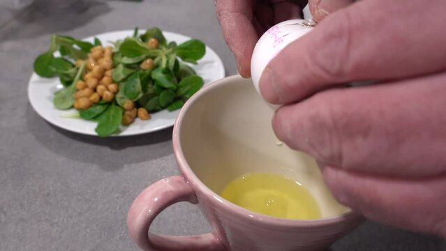 A male cook cracks an egg on a kitchen counter into a cup and separates the white from the yolk. 